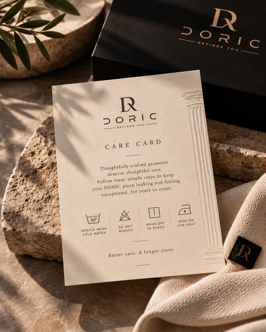 The DORIC care card with its washing symbols, on stone beside folded knitwear